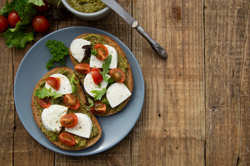Toast sandwich mozzarella cheese, cherry tomatoes and pesto bruschetta, toast on wooden background. Healthy breakfast, snack. Copy space.