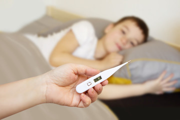 Obraz na płótnie Canvas female hand holds white thermometer on a blurred background with a lying boy, light background