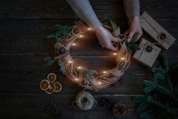 Christmas background with decorations, garland and pine cones. Creating wreath made of christmas tree branches and dry spice on dark vintage wooden board. Happy New Year. Toned image. Soft focus.