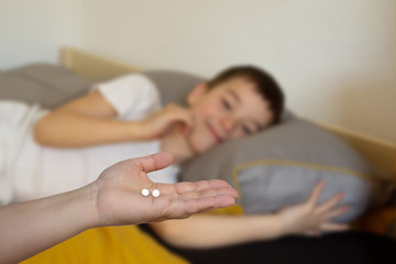 Obraz na płótnie Canvas female hand stretches on the palm two white pills on a blurred background of a lying boy, light background