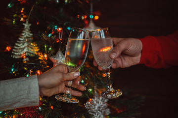 Two glasses of champagne raised in a toast against a Christmas tree glowing lights. Holiday and togetherness a family Christmas and Happy New Year. Party time. Couple with champagne. Selective focus.