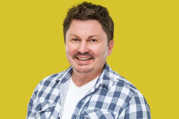 Portrait of happy successful handsome middle aged business man in casual checkered shirt, mustache standing and looking at camera with toothy smile. indoor studio shot, isolated on yellow background.