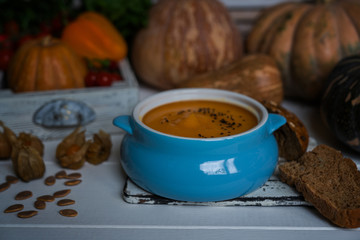 Pumpkin soup in a bowl with autumn vegetables and pumpkin seeds. Vegan soup. Vegetables cream soup and ingredients. Concept of healthy eating or vegetarian food. Toned image. Selective focus.