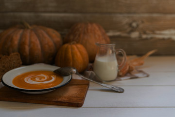 Homemade autumn butternut squash soup with bread. Roasted pumpkin and carrot soup with cream and pumpkin seeds on white wooden background. Concept of healthy eating food. Copy space. Toned image.