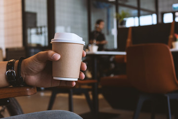 closeup hand holding paper cup of coffee in cafe with soft-focus and over light in the background