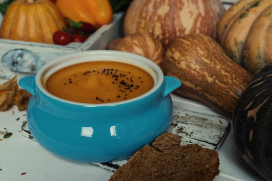 Pumpkin soup in a bowl with autumn vegetables and pumpkin seeds. Vegan soup. Vegetables cream soup and ingredients. Concept of healthy eating or vegetarian food. Toned image. Selective focus.