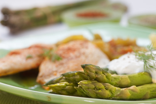 Roasted chicken breast meat and asparagus with sauce on green plate. Asparagus meal decorated with lemon and dill. Homemade cuisine. Close up image, shallow depth of field.