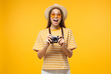 Happy surprised young female tourist holding camera, isolated on yellow background