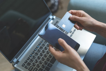 Young lady sitting in cafe and using smartphone, laptop and plastic bank card