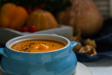 Homemade autumn butternut squash soup with bread. Roasted pumpkin and carrot soup with cream and pumpkin seeds on white wooden background. Concept of healthy eating food. Copy space. Toned image.