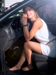 Fototapeta na wymiar Young beautiful woman lying on an automobile rudder, closing eyes and hugging it. Happy client of car dealership after purchase of vehicle.