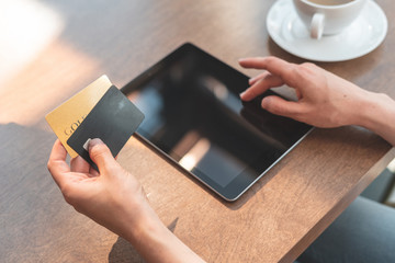 Young lady sitting in cafe and using tablet with credit card for online shopping