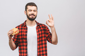 Young man holding a piece of hamburger. Student eats fast food. Burger is not helpful food. Very hungry guy. Diet concept isolated against white background. Ok sign.