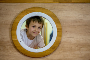 Sad little boy, looking through little round window of a submarine