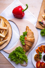 Top view of Homemade easy breakfast with fresh croissants, ham, red pepper and cheese on sandwich, tomato juice and cup of latte hot coffee on a wooden table.