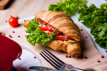Top view of Homemade easy breakfast with fresh croissants, ham, red pepper and cheese on sandwich, tomato juice and cup of latte hot coffee on a wooden table.