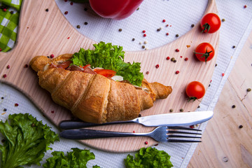 Top view of Homemade easy breakfast with fresh croissants, ham, red pepper and cheese on sandwich, tomato juice and cup of latte hot coffee on a wooden table.