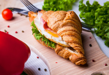 Top view of Homemade easy breakfast with fresh croissants, ham, red pepper and cheese on sandwich, tomato juice and cup of latte hot coffee on a wooden table.