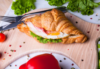 Top view of Homemade easy breakfast with fresh croissants, ham, red pepper and cheese on sandwich, tomato juice and cup of latte hot coffee on a wooden table.