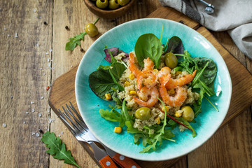 Diet menu, Vegan food. Healthy salad with quinoa, arugula, Shrimps and olives on a wooden rustic table. Copy space.