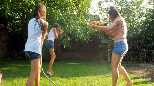 4k video of cheeruful laughing children with parent splashing water over each other from water guns and garden hose at backyard
