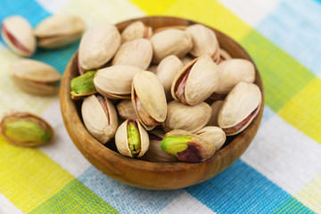 Pistachio nuts in small wooden bowl on checkered yellow cloth