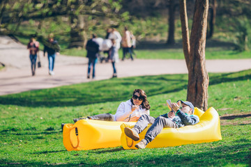 couple laying on yellow inflatable mattress in city park. reading book. drinking smoothies
