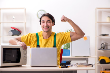 Young repairman repairing microwave in service centre 