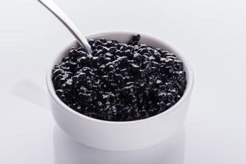 Fototapeta na wymiar black caviar in a bowl on a white acrylic background