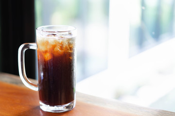 Closeup glass of ice americano coffee on wood table with green nature background, selective focus