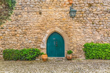 View of the medieval gate door on Luso Roman castle of Óbidos, with ceramic pot with plants, in Portugal