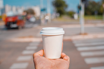 Hand holding paper cup with take out coffee at pedestrian walk on street
