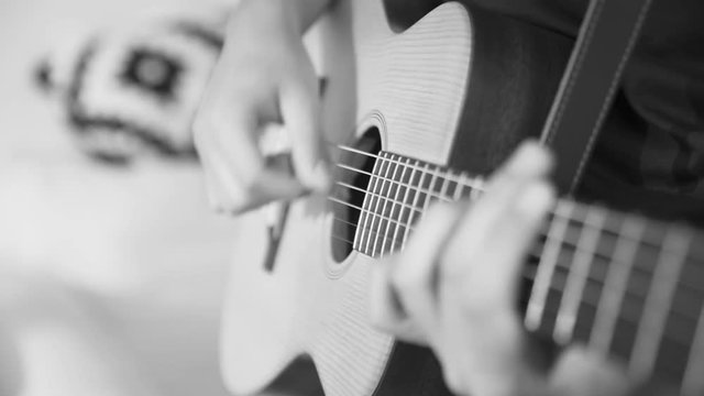 black and white closeup shot of hands of a male musician plucking a guitar