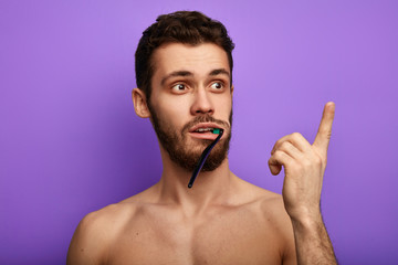 funny guy with toothbrush in the mouth pointing at copy space. close up photo.puzzled emotional man pointing at somewhere.