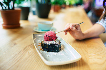Smiling young Woman eating chocolate cake with berry ice-cream and cup of coffee in cafe