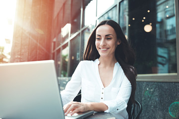 Happy beautiful young businesswoman working on laptop in street cafe outdoor