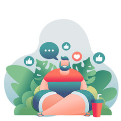 Young modern guy downshifter sits on the beach with a laptop on the background of palm trees.