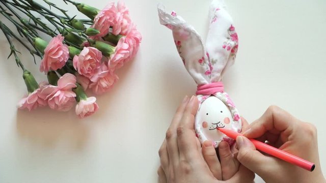 Women's and children's hands hold chicken egg decorated for Easter bunny, paint rabbit's face with pink marker. Handmade Easter design