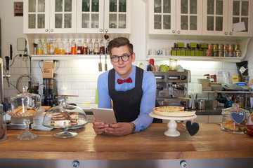 Handsome small business owner businessman standing behind the counter and waiting for guest