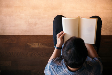 Young man reading book while sitting in the library, over shoulder view with soft focus with copy space,warm retro tone.