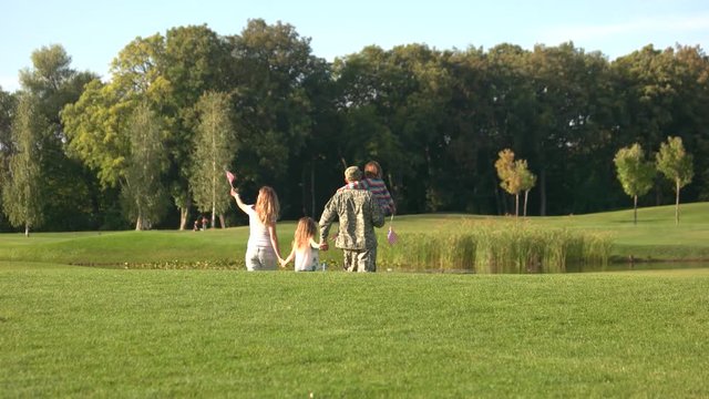 US veteran in camoubackgrounde with family walking away. Family walking forward on the grass on golf course.