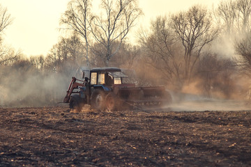 Sowing time. Blue tractor rides through the agricultural field in the sunlight.