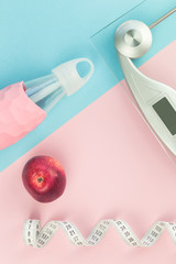 Blue tape measure with weighing scale, trendy glass water bottle and red apple on pink blue background in flat lay with copy space. Weight management and healthy lifestyle concept