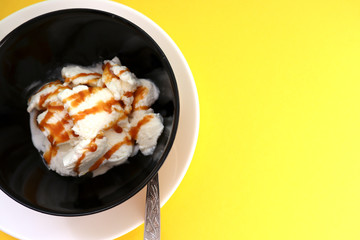 Vanilla ice cream in black bowl on yellow background