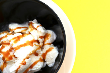 Vanilla ice cream in black bowl on yellow background
