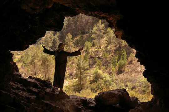 MAN WITH DJELLABA AND PALESTINIAN SCARF IN A CAVE LOOKING TO THE VALLEY WITH OPEN ARMS