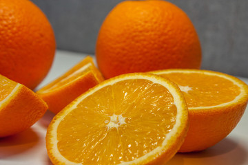 A sliced juicy orange and two whole oranges close-up against a gray wall.