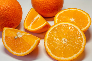 Top view of a cut into four pieces of juicy orange and two whole oranges close-up on a white background.