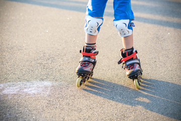 Plakat Little boy learning to roller skate in summer park. Children wearing protection pads for safe roller skating ride. Active outdoor sport for kids. Close up view of skates