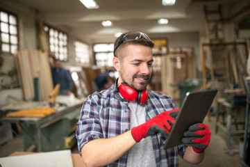 Portrait of casual middle aged worker carpenter with tablet in carpentry workshop.